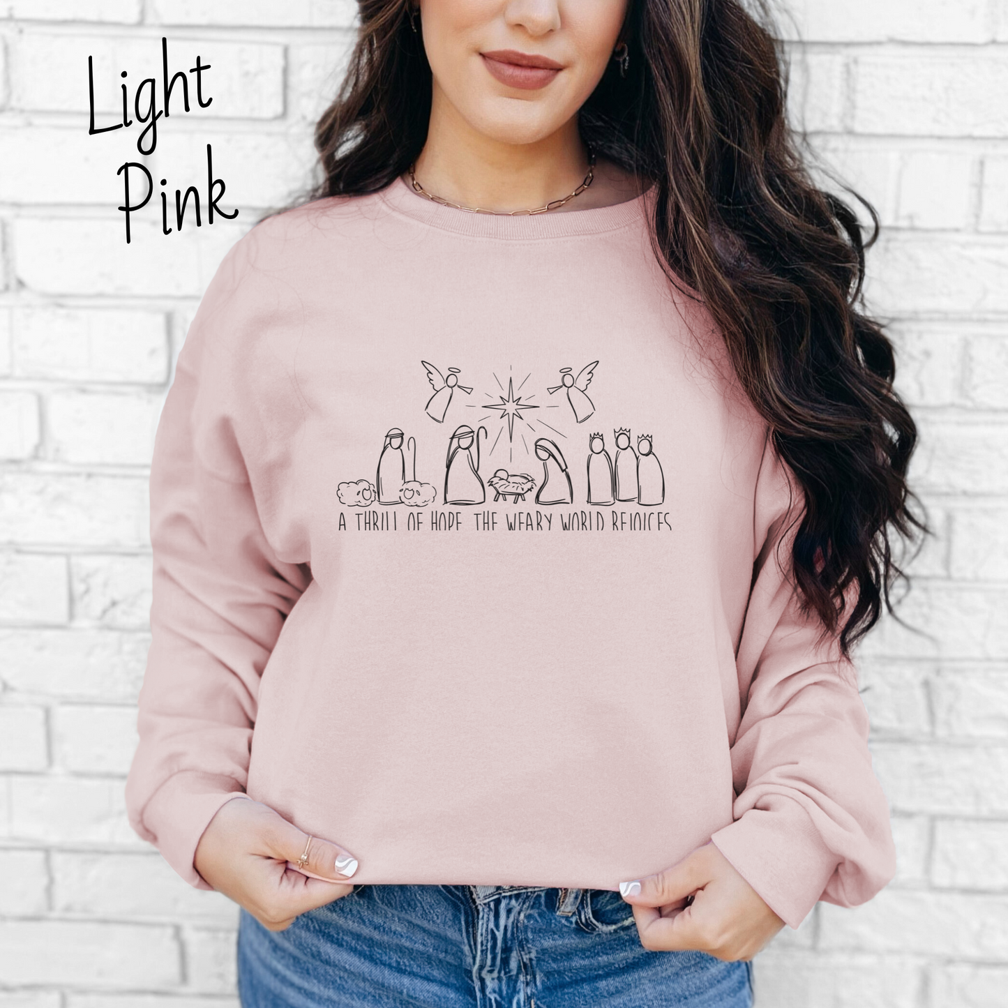 Hand drawn nativity scene with the words "A thrill of hope, the weary world rejoices" written underneith. Design is black on a light pink colored sweatshirt.