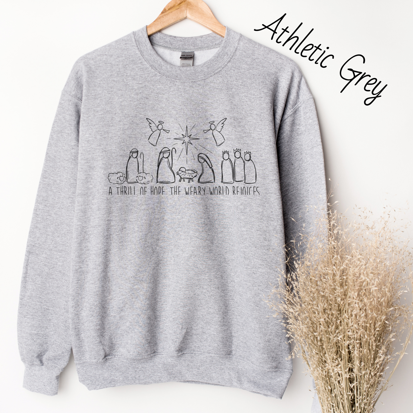 Hand drawn nativity scene with the words "A thrill of hope, the weary world rejoices" written underneith. Design is black on a light grey colored sweatshirt.