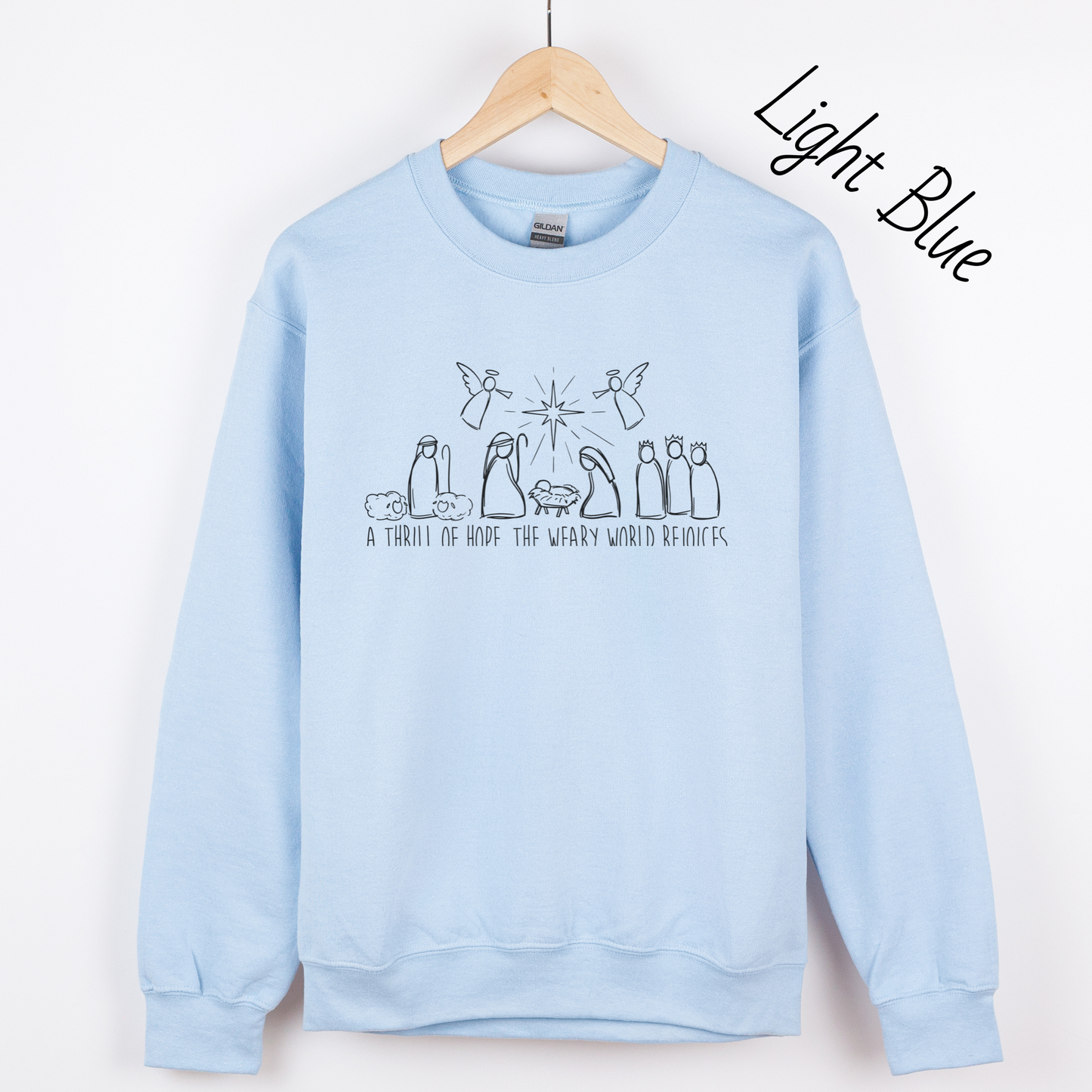 Hand drawn nativity scene with the words "A thrill of hope, the weary world rejoices" written underneith. Design is black on a light blue sweatshirt.
