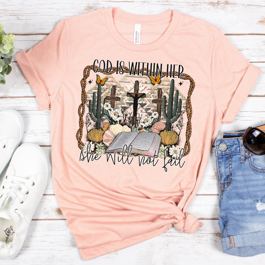 The God Is Within Her Western Short Sleeve Tee features a buttery soft design made from Airlume cotton. Its pink motif displays crosses, cacti, flowers, and butterflies with the quote God is within her, she will not fail, ideal with white sneakers and denim shorts on a wooden background.