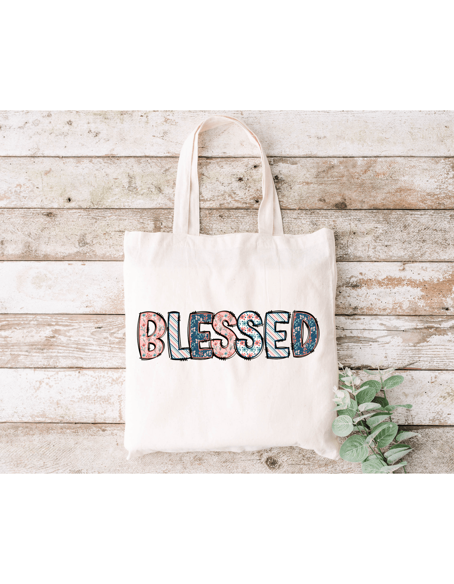 The Blessed (Spring Floral) canvas bag in beige sits on a rustic wooden background with a small green plant at the lower right, ideal for carrying essentials to Bible study.