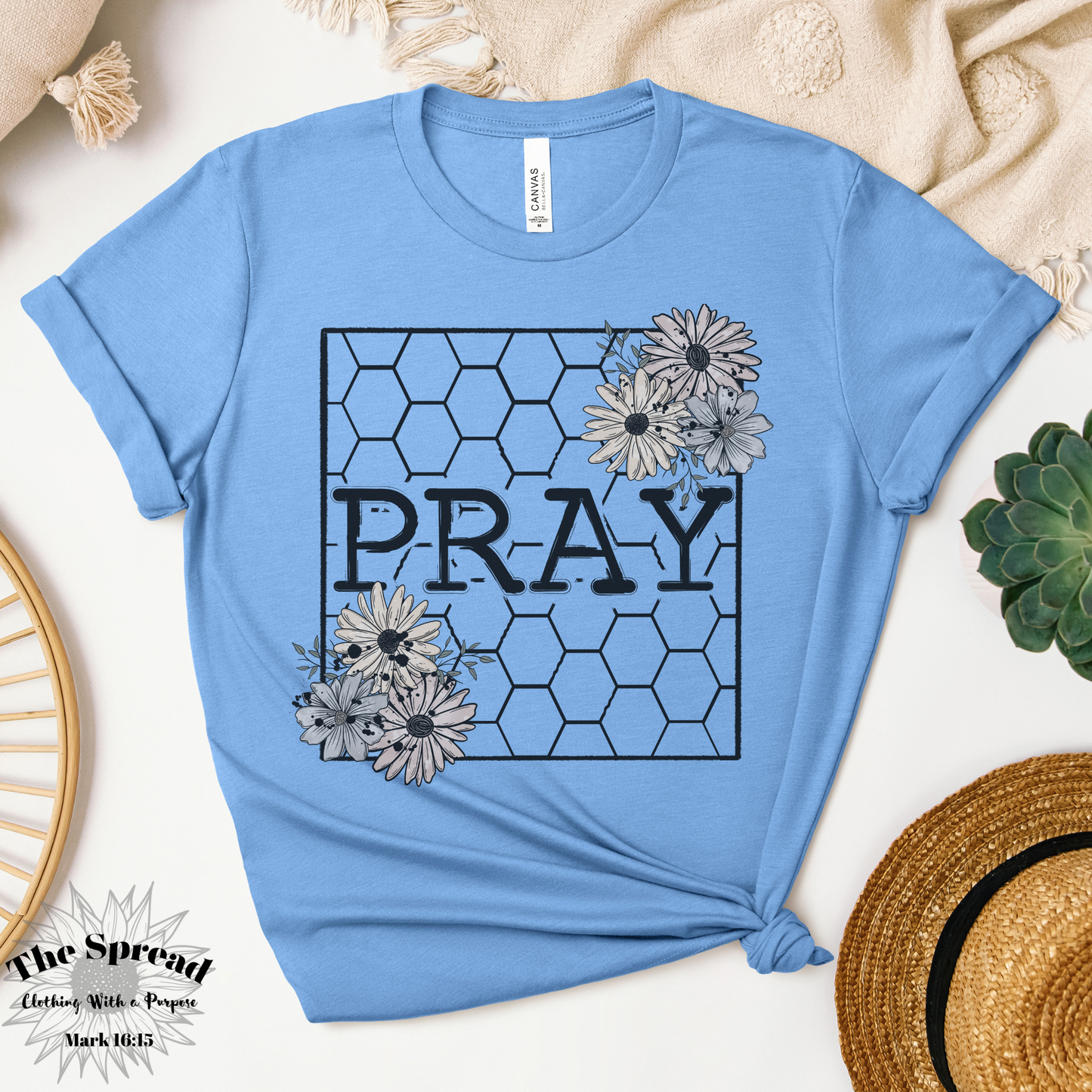 The Pray Honeycomb Short Sleeve Tee, a pine colored t-shirt made from Airlume combed cotton, features PRAY in bold within a honeycomb pattern. Floral designs accent the corners.