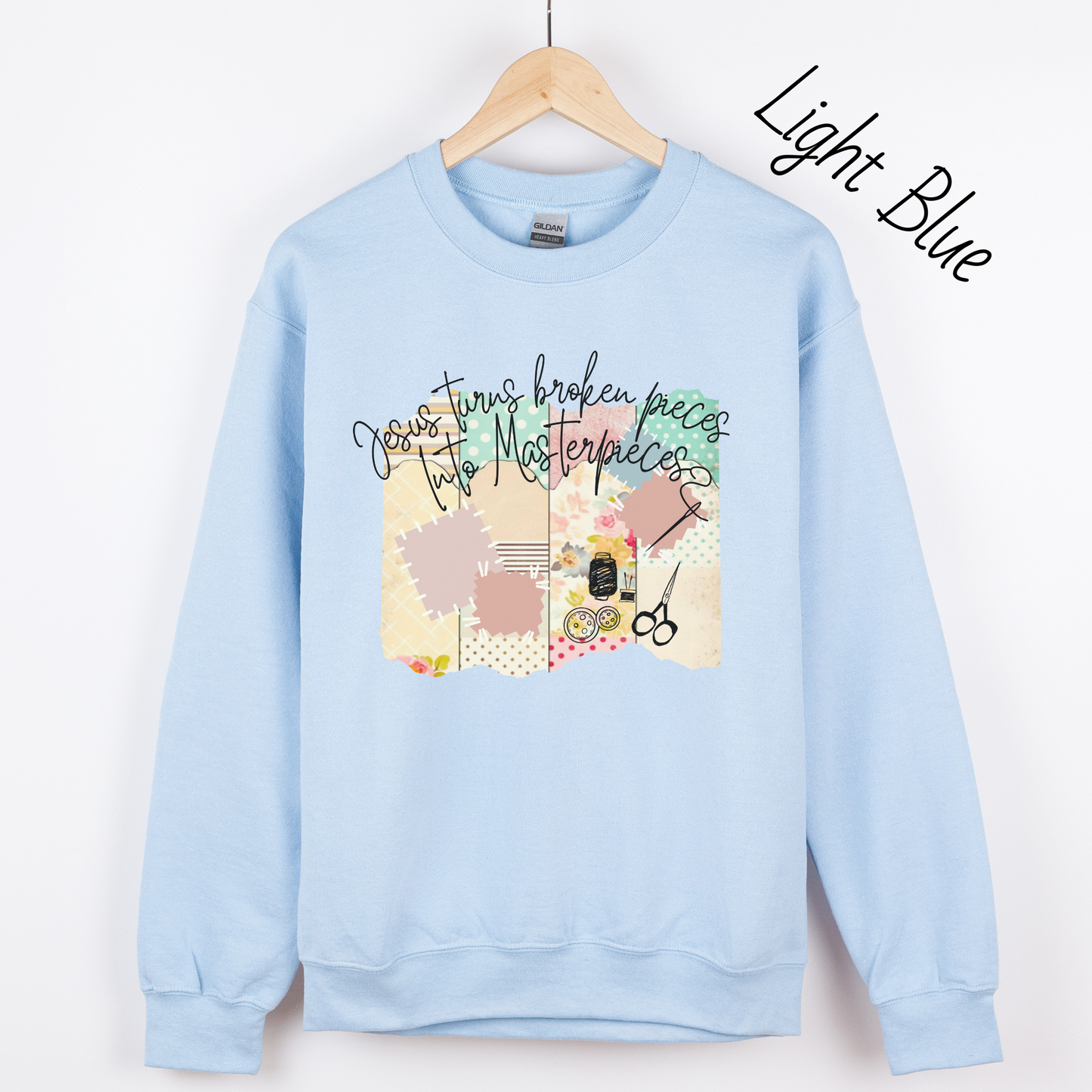 Light blue sweatshirt with multicolored quilt design with the words "Jesus turns broken pieces into masterpieces written across the top in black cursive script.