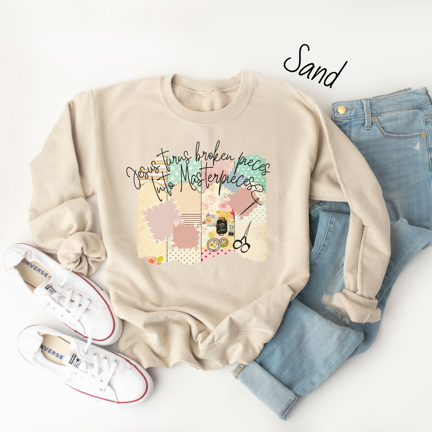 Sand colored sweatshirt with multicolored quilt design with the words "Jesus turns broken pieces into masterpieces written across the top in black cursive script.