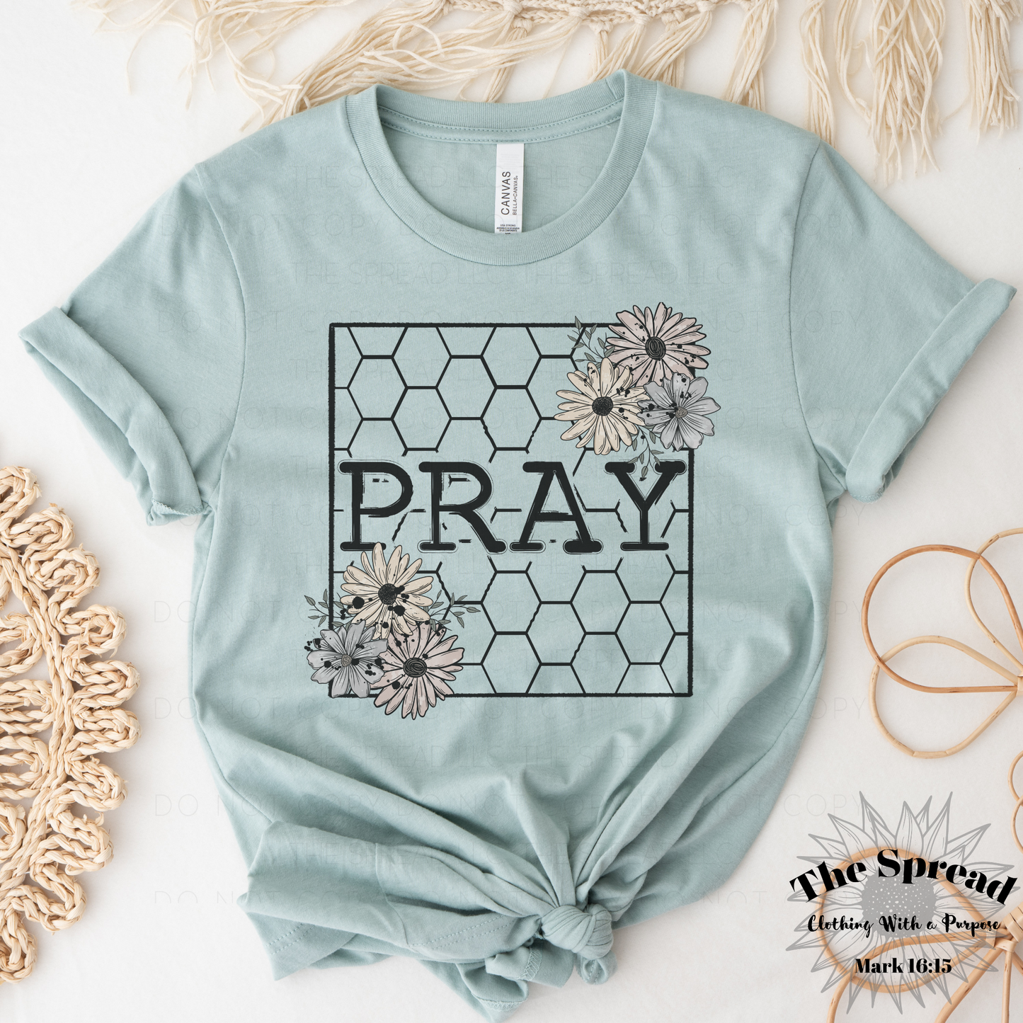 The Pray Honeycomb Short Sleeve Tee, a heather sage t-shirt made from Airlume combed cotton, features PRAY in bold within a honeycomb pattern. Floral designs accent the corners.