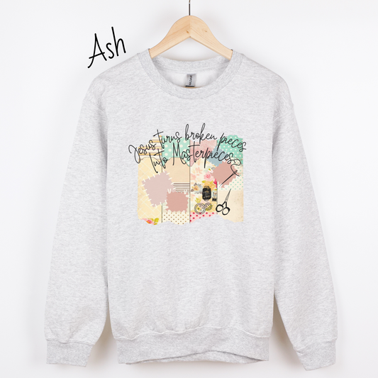 Ash colored sweatshirt with multicolored quilt design with the words "Jesus turns broken pieces into masterpieces written across the top in black cursive script.