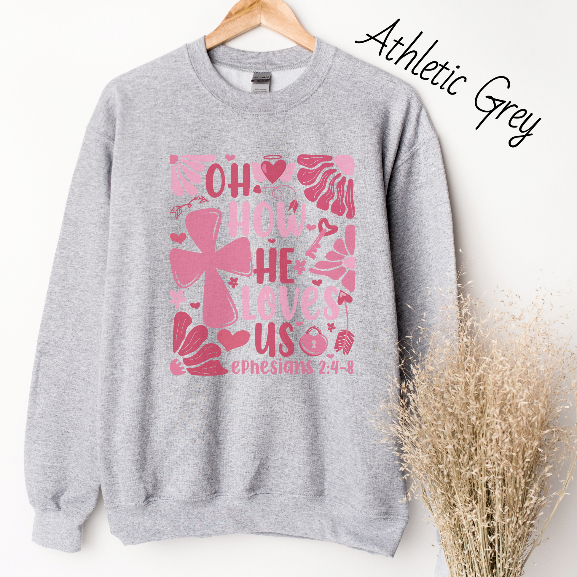 "Oh how He loves us Ephesians 2:4-8" written in various shades of pink with florals and a cross on a light grey sweatshirt.