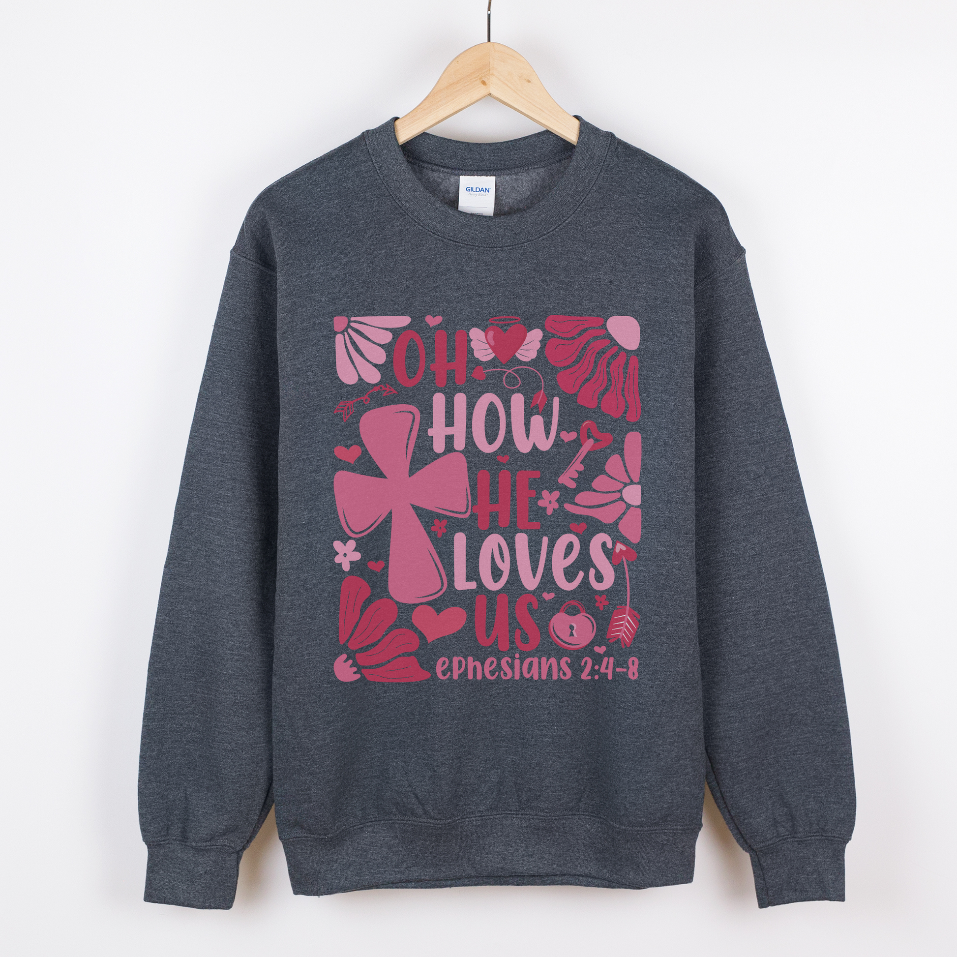 "Oh how He loves us Ephesians 2:4-8" written in various shades of pink with florals and a cross on a dark grey sweatshirt.