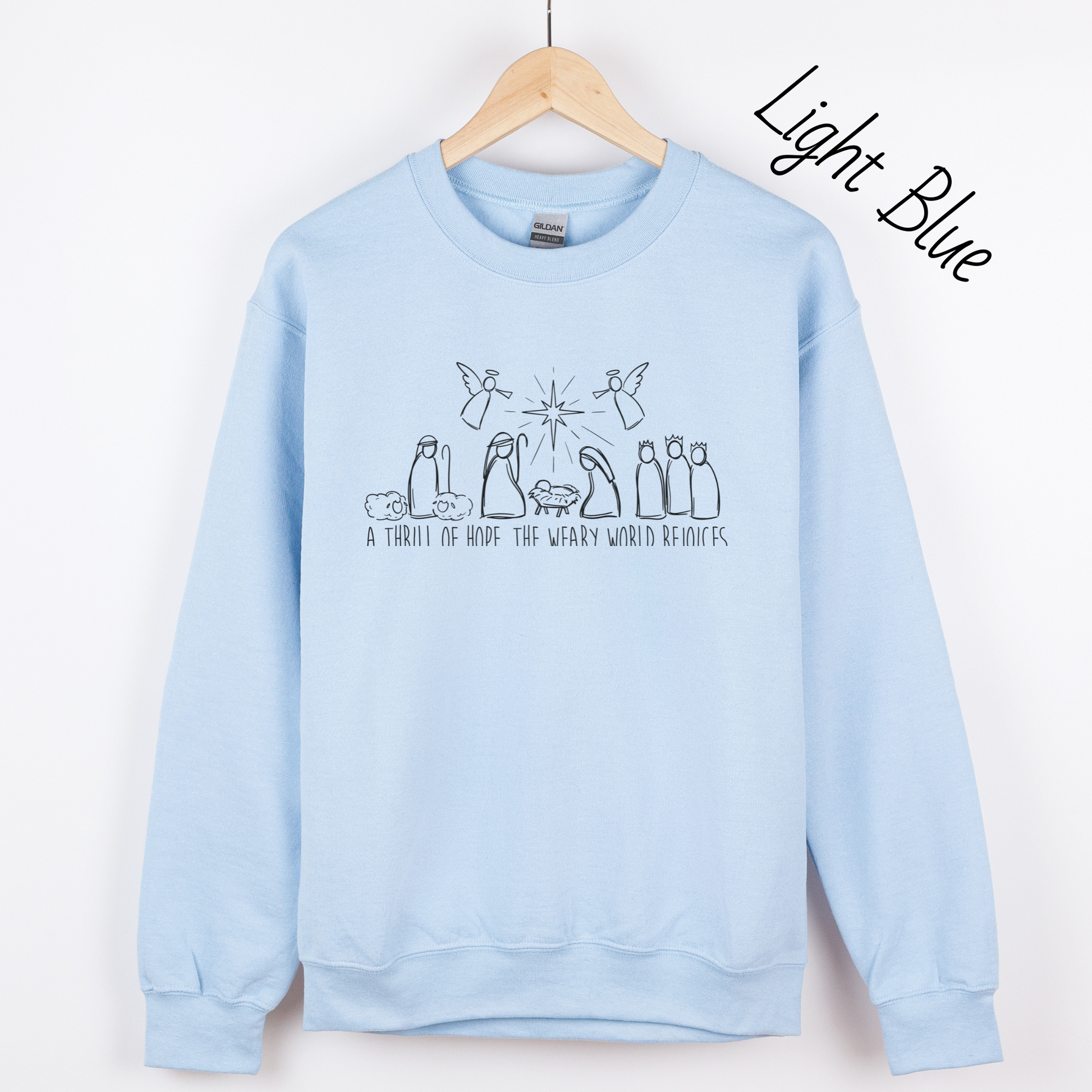 Hand drawn nativity scene with the words "A thrill of hope, the weary world rejoices" written underneith. Design is black on a light blue sweatshirt.