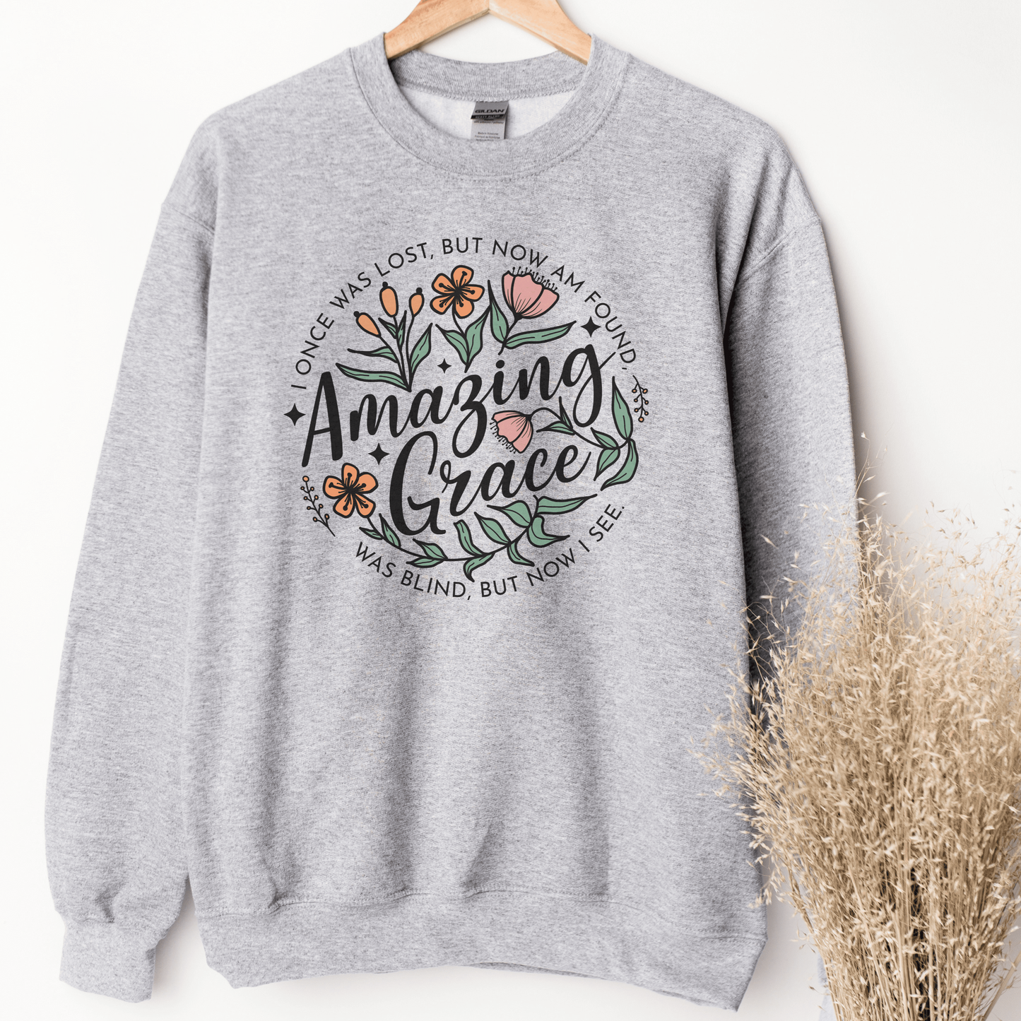 Words "Amazing Grace" with florals around and "I once was lost but now am found, was blind but now I see" in a circle around the main design. Design is on a light grey colored sweatshit.