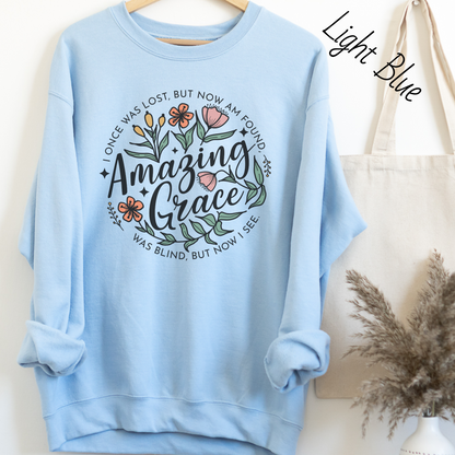 Words "Amazing Grace" with florals around and "I once was lost but now am found, was blind but now I see" in a circle around the main design. Design is on a light blue colored sweatshit.