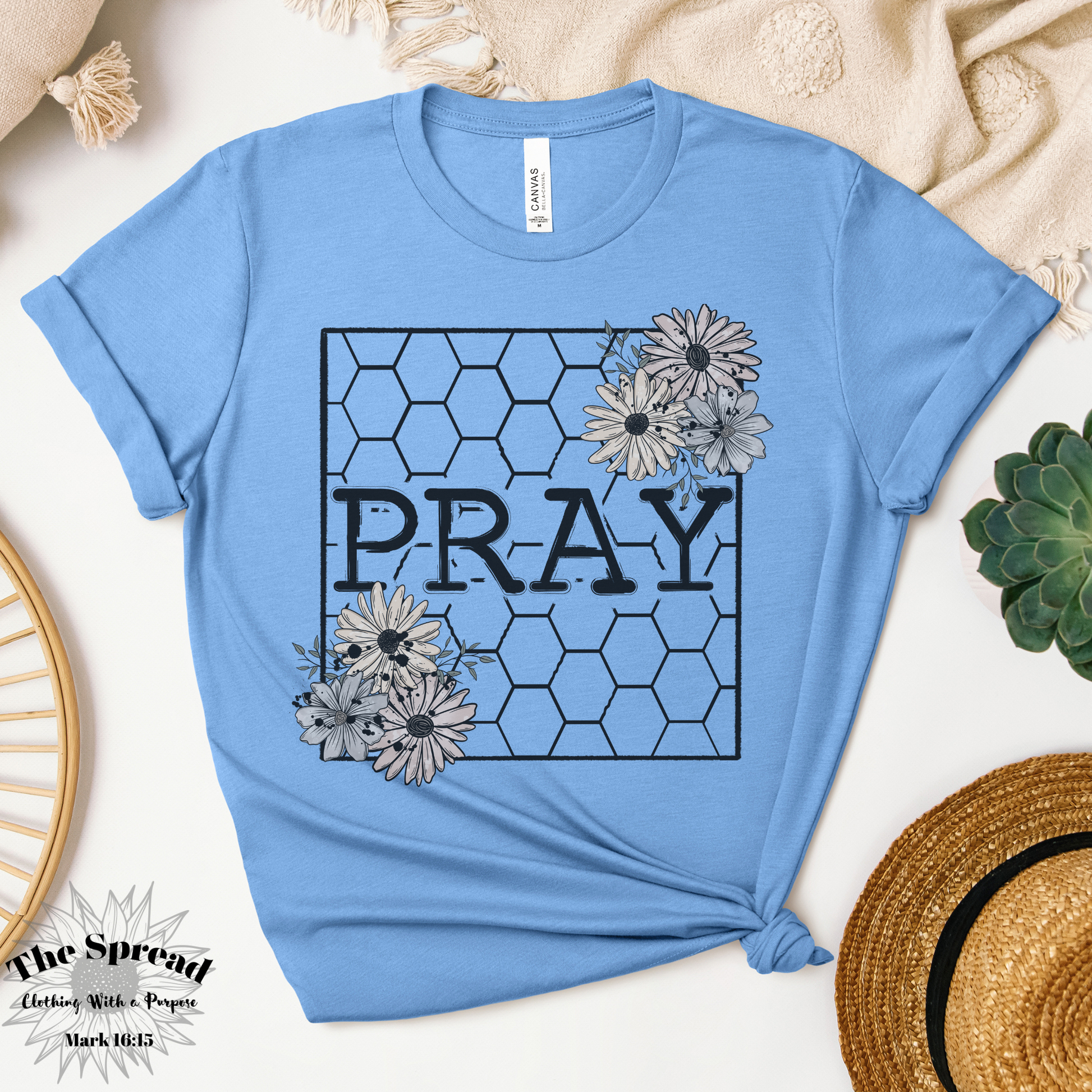 The Pray Honeycomb Short Sleeve Tee, a pine colored t-shirt made from Airlume combed cotton, features PRAY in bold within a honeycomb pattern. Floral designs accent the corners.