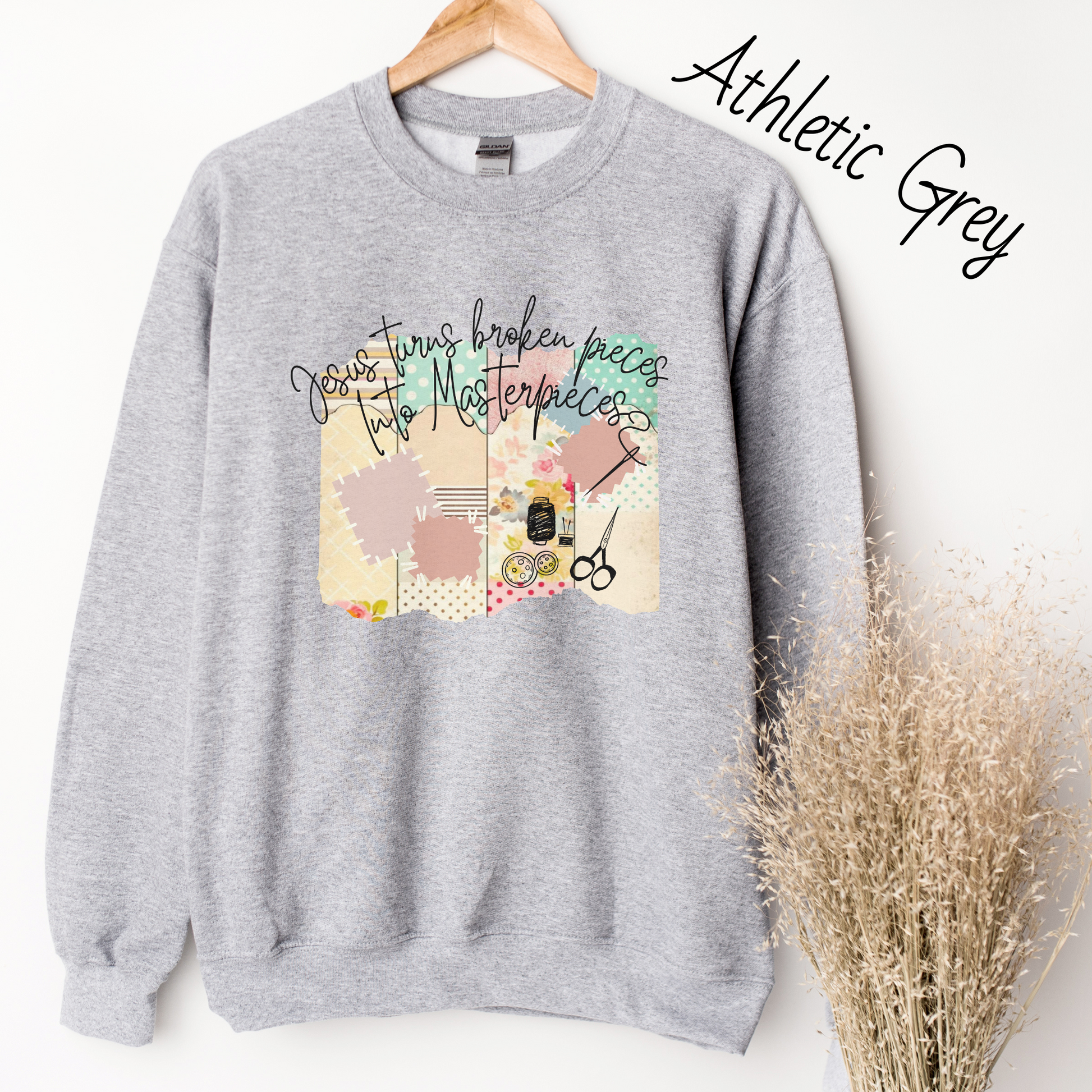 Light grey sweatshirt with  multicolored quilt design with the words "Jesus turns broken pieces into masterpieces written across the top in black cursive script. 