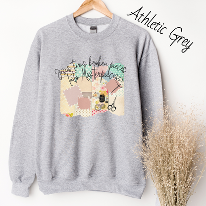 Light grey sweatshirt with  multicolored quilt design with the words "Jesus turns broken pieces into masterpieces written across the top in black cursive script. 
